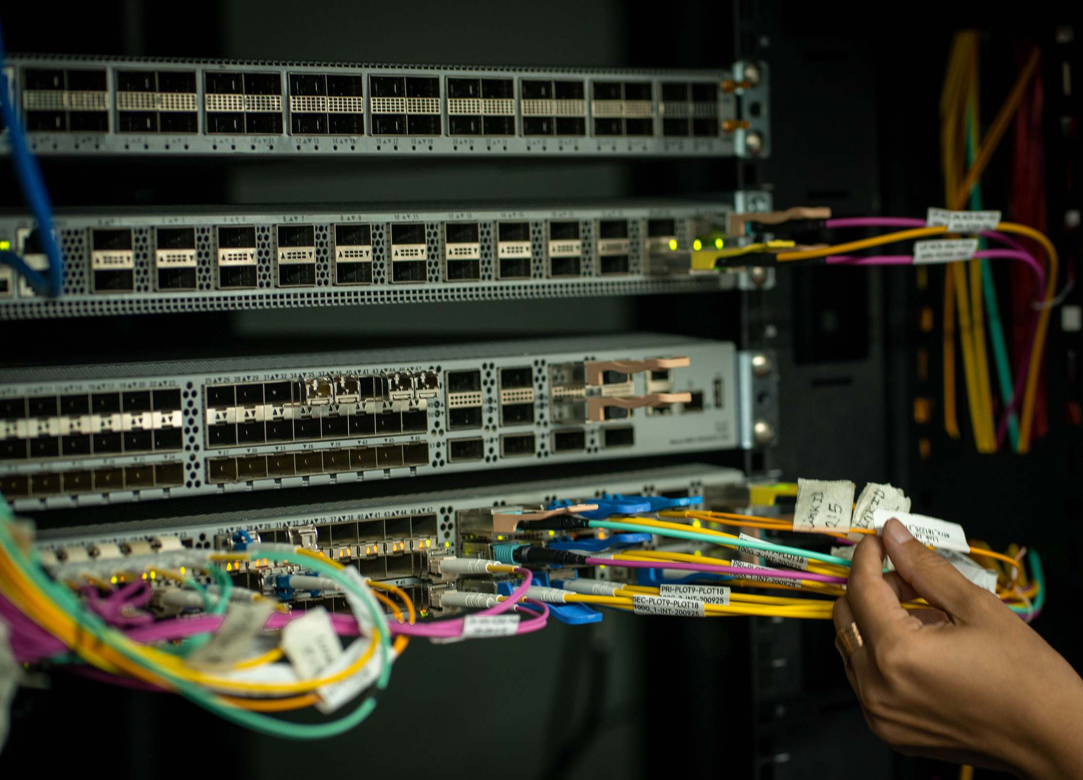 Hands managing fiber optic cables in a server room datacenter